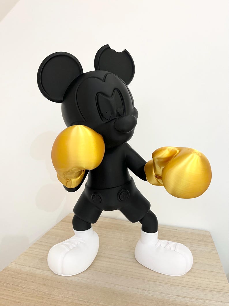 Puede incluir: Figura negra de Mickey Mouse con guantes de boxeo dorados y zapatos blancos. La figura tiene una mordida en una oreja. La figura est&aacute; en posici&oacute;n de boxeo.