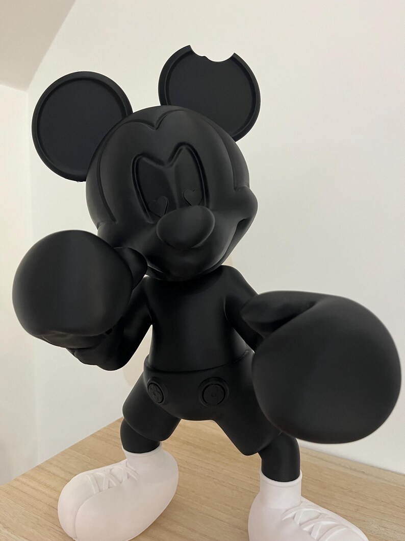 Puede incluir: Una figura negra de Mickey Mouse en posici&oacute;n de boxeo, con grandes guantes de boxeo negros y zapatos blancos. La figura tiene un acabado mate y est&aacute; posada con los brazos en alto, lista para pelear. Las orejas son redondas, y una oreja tiene una mordida.