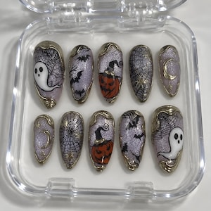 May include: A set of ten almond-shaped press-on nails featuring a lavender glitter base with gold metallic edges. Designs include white ghosts, black spiderwebs, orange jack-o'-lanterns, black bats, and gold crescent moons with stars.
