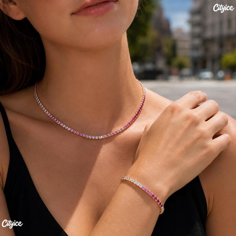 May include: A tennis necklace and a matching tennis bracelet featuring a gradient of round-cut stones that transition from clear white to vibrant pink. Both pieces are set in a metallic finish and worn against a black top with Cityice branding.