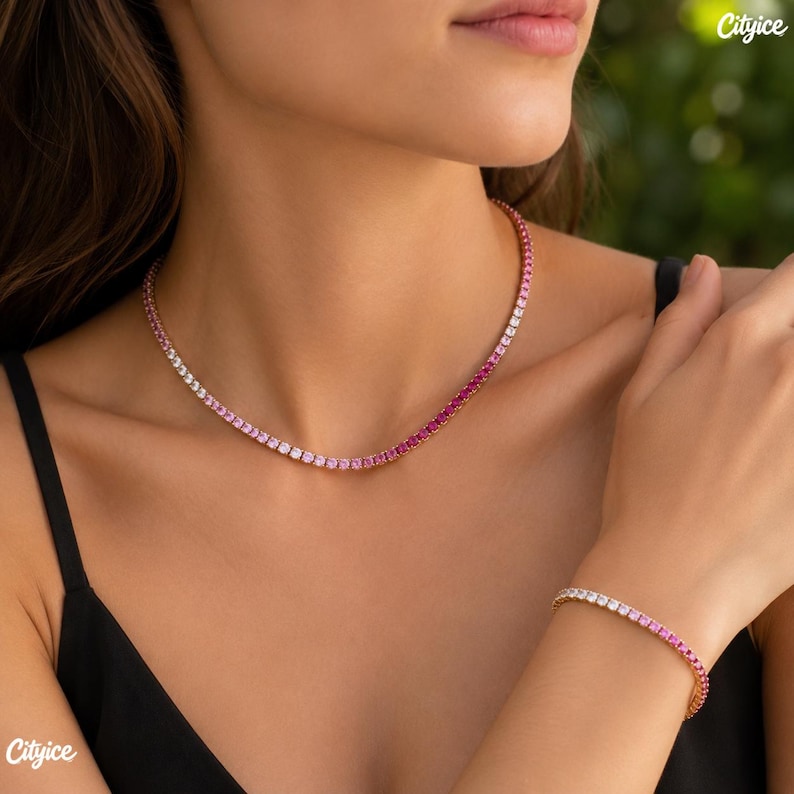 May include: A tennis necklace and a matching tennis bracelet featuring a gradient of round-cut stones that transition in color from clear white to light pink and deep magenta, set in a metallic frame worn around the neck and on the wrist.