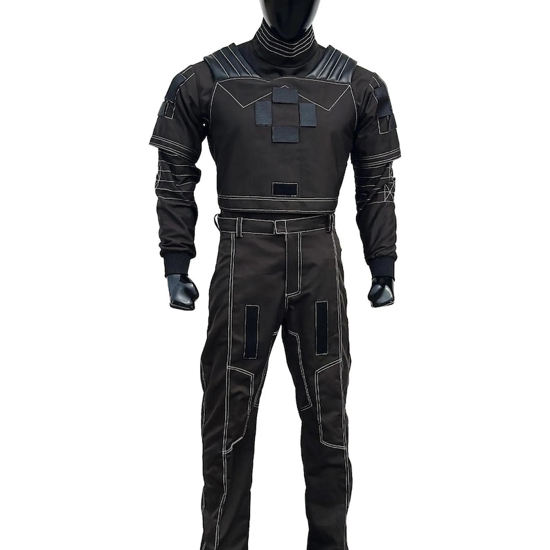 May include: Black jumpsuit with white stitching details. The outfit features a high collar, padded shoulders, and a belt. The long-sleeved top has a geometric design on the chest. The pants have rectangular patches and a straight leg design.