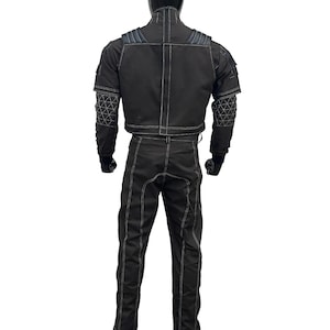 May include: Black racing suit with white stitching. The suit includes a jacket with padded shoulders and geometric patterned accents on the sleeves, and matching pants. The suit is designed for motorsports.