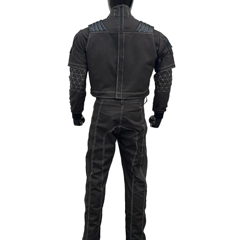 May include: Black racing suit with white stitching. The suit includes a jacket with padded shoulders and geometric patterned accents on the sleeves, and matching pants. The suit is designed for motorsports.