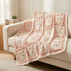 Puede incluir: Una manta de ganchillo compuesta por paneles cuadrados con caras de conejo en relieve tridimensional. La manta está elaborada en tonos crema, rosa suave y blanco, con un borde festoneado y detalles de punto de burbuja por toda la pieza.
