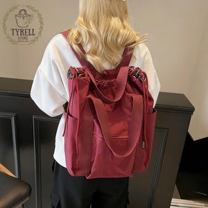 Może przedstawiać: Bordowa torba typu tote z plecakiem, ze ściągaczem i paskami na ramiona. Torba ma dwie boczne kieszenie i przednią kieszeń. Torba ma logo TYRELL STORE w lewym górnym rogu.