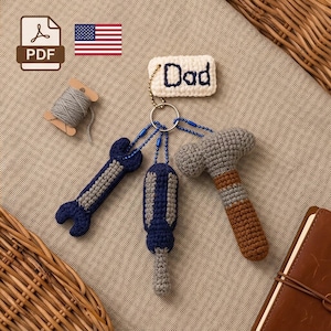 May include: A crochet keychain set featuring a rectangular white tag with the word Dad embroidered in dark blue, attached to a metal ring with three small crocheted tools: a dark blue wrench, a dark blue and gray screwdriver, and a gray and brown hammer.