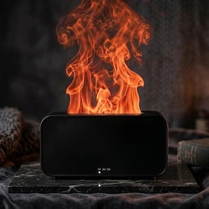 May include: A black rectangular aromatherapy diffuser with a flame effect. The diffuser emits an orange and red flame-like light. The control panel has 1H, 3H, and SH settings. The diffuser sits on a dark marble surface.