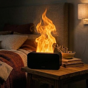 Può includere: Un dispositivo nero rettangolare con effetto fiamma che emette fiammate arancioni e gialle brillanti. Il dispositivo è posizionato su un comodino di legno accanto a un letto con una coperta e cuscini fantasia. Un'applique fornisce un'illuminazione soffusa.