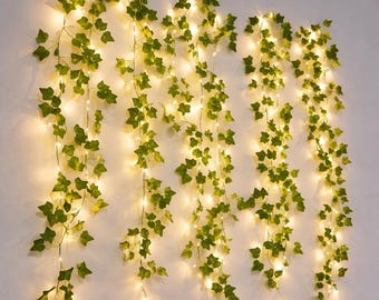 May include: Artificial ivy garland with small, warm white LED lights. The green leaves are arranged along a thin wire, creating a decorative vine effect. The lights are evenly spaced, providing a soft glow. Ideal for home decor or event decoration.