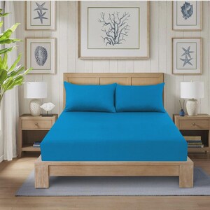 Pode incluir: Uma cama com estrutura de madeira clara e um lençol azul brilhante e duas fronhas a condizer. O quarto tem um tema costeiro com arte emoldurada e mesas de cabeceira com candeeiros.