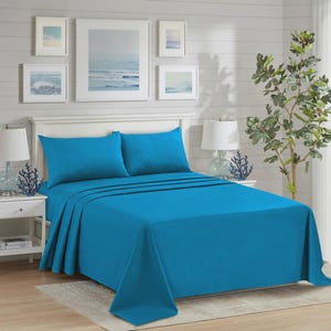 Può includere: Un letto è fatto con un set di lenzuola turchese brillante, tra cui un lenzuolo piano, un lenzuolo con angoli e due federe. Il letto è contro un muro bianco con opere d'arte a tema oceanico incorniciate. Due comodini bianchi con lampade e coralli sono visibili.