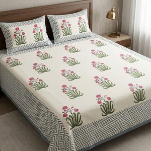 Può includere: Un set di lenzuola con base color bianco sporco e un motivo ripetuto di fiori rosa con steli verdi. I bordi del lenzuolo e delle due federe sono decorati con un motivo a chevron grigio e bianco su uno sfondo di colore grigio uniforme.
