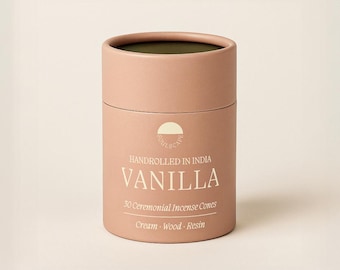 May include: A cylindrical, light pink container of vanilla incense cones. The container has a dark brown interior and features the text "Handrolled in India" and "Vanilla". It also states "30 Ceremonial Incense Cones" and lists "Cream - Wood - Resin".