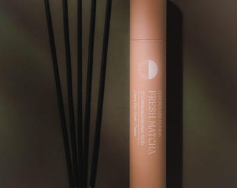 May include: A cylindrical peach-colored cardboard tube labeled Fresh Matcha with 20 ceremonial incense sticks, alongside five thin black incense sticks with yellow wooden ends. The text reads Handrolled in India, Fresh Matcha, 20 Ceremonial Incense Sticks, Green Tea, Herb, Cream.