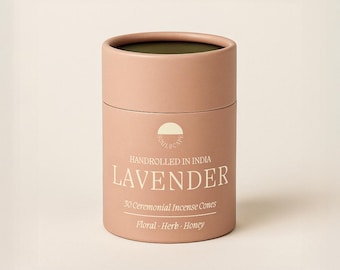 May include: A cylindrical, light pink container of lavender incense cones. The container has a white label with the word "LAVENDER" in large font. The label also states "Handrolled in India" and "30 Ceremonial Incense Cones". The bottom of the label lists "Floral - Herb - Honey".
