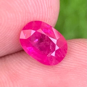 Op de afbeelding: Een levendige, ovaal geslepen edelsteen met een diepe, verzadigde felroze kleur. De steen heeft een gefacetteerd oppervlak dat licht reflecteert, wat zorgt voor een briljante, sprankelende uitstraling met duidelijke geometrische patronen.