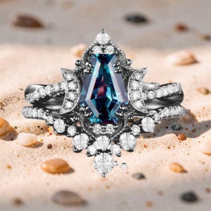 Puede incluir: Un conjunto de dos anillos con una gran piedra preciosa de color verde azulado y piedras más pequeñas y claras. Los anillos tienen una banda de metal oscuro, uno con un diseño retorcido y el otro con un engaste decorativo.