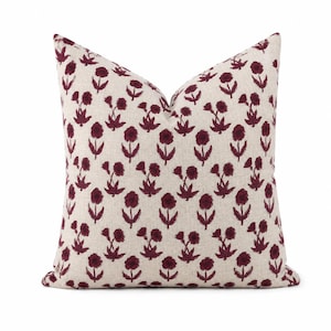 May include: A square throw cushion featuring a light beige, textured fabric base with a repeating pattern of dark maroon, hand-drawn style floral motifs. The flowers are arranged in a consistent grid, each with a stem and two leaves.