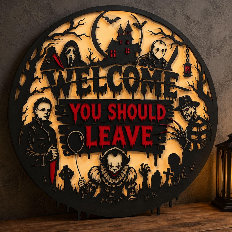 May include: A circular black wooden wall sign with a backlit yellow background featuring horror movie characters. The text reads WELCOME YOU SHOULD LEAVE in black and red. It depicts figures including a clown, a masked slasher, and a haunted house.