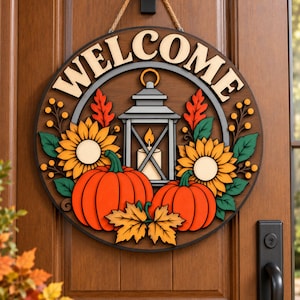 May include: A circular wooden door sign featuring the word WELCOME in raised cream letters. The design includes a central grey lantern with a lit candle, flanked by two large yellow sunflowers, two orange pumpkins, and green leaves.