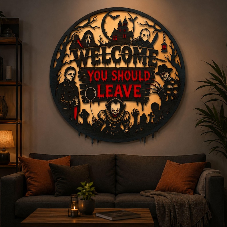 May include: A circular black wall sign featuring a backlit horror-themed design with the text "WELCOME YOU SHOULD LEAVE" in red and black. The artwork includes silhouettes of iconic horror movie characters, a haunted house, and a graveyard.
