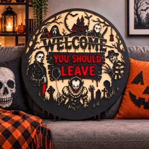 May include: A circular wooden wall sign featuring layered horror movie characters including Michael Myers, Jason Voorhees, Freddy Krueger, and Pennywise. The text reads "WELCOME" in black and "YOU SHOULD LEAVE" in red against a light wood background.