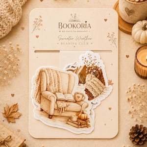 May include: A beige display card labeled BOOKORIA SEE YOU IN THE MOONLIGHT Sweater Weather READING CLUB featuring die-cut stickers of a cozy armchair with a knit throw, an open book, a mug, a candle, and a pumpkin in warm brown tones.