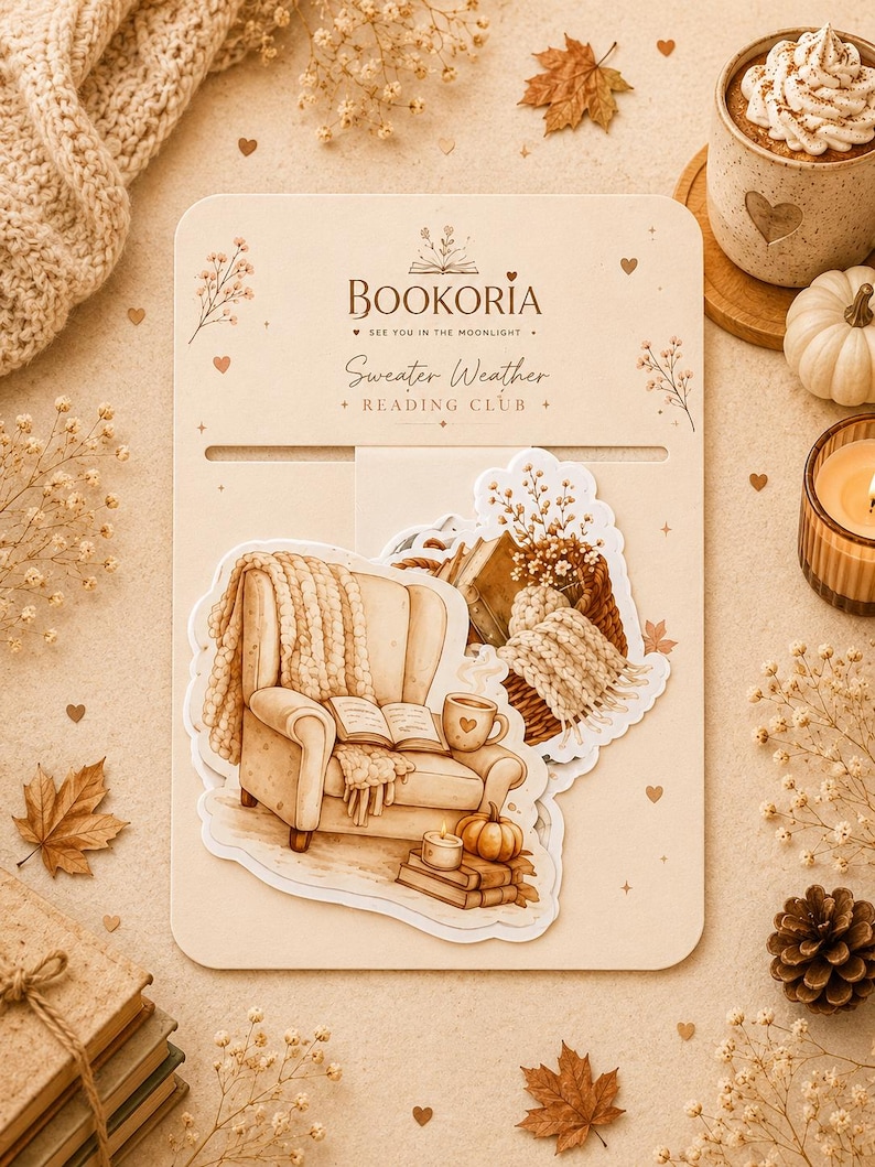 May include: A beige display card labeled BOOKORIA SEE YOU IN THE MOONLIGHT Sweater Weather READING CLUB featuring die-cut stickers of a cozy armchair with a knit throw, an open book, a mug, a candle, and a pumpkin in warm brown tones.