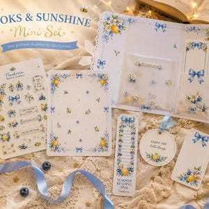Könnte beinhalten: Ein Schreibwaren-Set mit dem Titel Books & Sunshine Mini Set, bestehend aus einer Mappe, einem Stickerbogen und Anhängern, verziert mit blauen Schleifen, gelben Zitronen und weißen Blüten. Enthalten sind ein Lesezeichen mit der Aufschrift Summer Reading 2026, ein runder Anhänger mit dem Text Enjoy the little things sowie weitere Papieraccessoires.