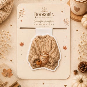 May include: A beige sweater-shaped sticker on a rectangular backing card. The sticker features a chunky knit sweater holding a mug labeled Pumpkin Latte and a small pumpkin. The card displays the text Bookoria Sweater Weather Reading Club.