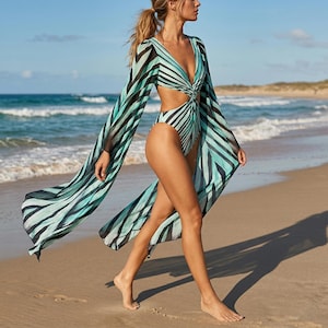 Puede incluir: Un bañador de una pieza con una cubierta a juego. El bañador y la cubierta presentan un estampado de rayas en negro y tonos turquesa. El bañador tiene un escote en V profundo y un detalle recortado en la cintura. La cubierta tiene mangas largas y fluidas.