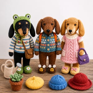 May include: Three knitted stuffed animal figures resembling dogs. The left dog wears a green frog hat and striped sweater with a brown bag. The center dog wears a patterned cardigan. The right dog wears a pink cable-knit dress and purple purse.