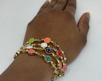 Peut inclure: Un bracelet en or avec plusieurs rangs de petites perles et des breloques souriantes colorées. Le bracelet est porté au poignet.
