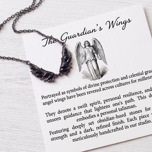 Puede incluir: Un collar oscuro, con un tono de metal de ca&ntilde;&oacute;n, con un colgante en forma de ala con piedras de color obsidiana. El collar se muestra con una tarjeta que dice "The Guardian's Wings" y describe el simbolismo de las alas de &aacute;ngel.