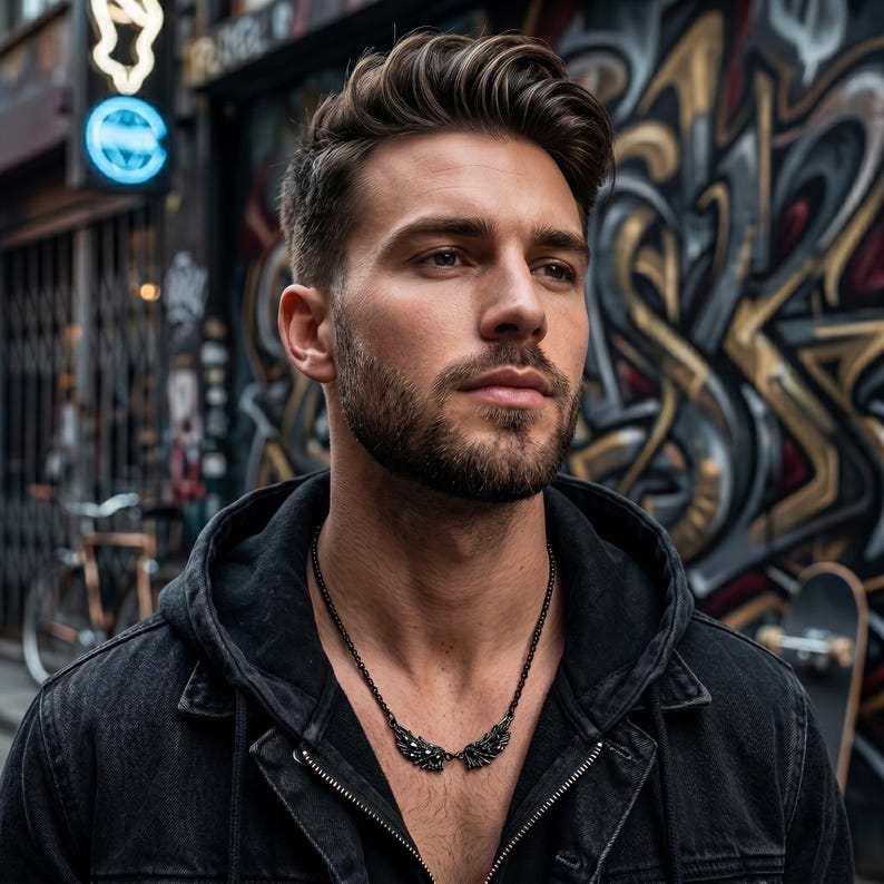 Puede incluir: Un collar negro con un dise&ntilde;o de alas. El collar lo lleva una persona con una chaqueta con capucha negra. El fondo presenta arte de graffiti y una escena callejera borrosa.