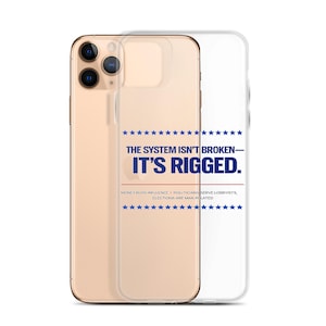 May include: A clear phone case with a gold phone inside. The case has the text "THE SYSTEM ISN'T BROKEN - IT'S RIGGED." in blue and white. The text is surrounded by blue stars. The phone case is a political statement.