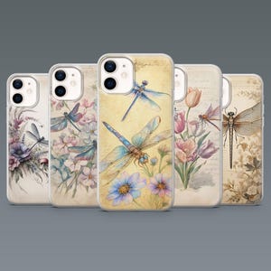 May include: A collection of five phone cases with dragonfly and floral designs. The cases feature watercolor illustrations of dragonflies, flowers, and foliage in shades of blue, pink, and beige. The cases are made of clear plastic.