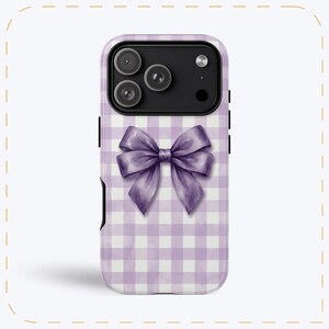 Pode incluir: Capa de telemóvel com um laço roxo num padrão vichy lilás e branco. A capa tem um módulo de câmara preto e botões laterais pretos. O laço é um design em aquarela.