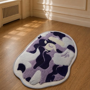Può includere: Un tappeto di forma ovale con un motivo mimetico astratto nei toni del blu navy profondo, lavanda chiaro e bianco tenue. Il tappeto presenta una superficie in pelo trapuntato testurizzato ed è rifinito con un bordo azzurro.