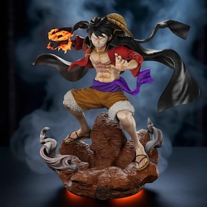 Può includere: Statuetta dettagliata di un personaggio della serie anime One Piece. La figura è in posa dinamica, con un cappello di paglia, una giacca rossa e pantaloncini marroni. La figura è su una base rocciosa con effetti di fuoco.