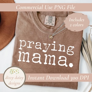 Może przedstawiać: Brązowa koszulka z napisem "praying mama" w białych literach. Koszulka ma okrągły dekolt i krótkie rękawy. Obraz zawiera również tekst "Commercial Use PNG File", "Includes 2 colors", "Instant Download 300 DPI" oraz logo "dizzy daisy designs".