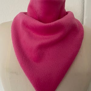 Peut inclure: Un foulard triangulaire rose vif fabriqué dans un tissu doux, pelucheux et duveteux. Le foulard est drapé autour du cou d'un mannequin, présentant un design frontal pointu qui tombe en forme de V, couvrant entièrement la zone du cou.