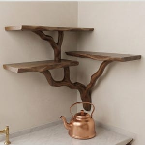 Op de afbeelding: Een hoekplank van hout met drie niveaus en een takontwerp. De planken zijn rechthoekig met een natuurlijke rand, ondersteund door een gesneden houten structuur. Een koperen theepot staat eronder.