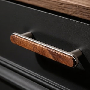 May include: Close-up of a black cabinet with two drawers. Each drawer features a brushed metal handle with a rectangular, wood-grain center. The top of the cabinet is a light brown wood.