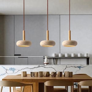 Może przedstawiać: Trzy lampy wiszące o naturalnym, minimalistycznym designie. Każda lampa ma beżowy, okrągły klosz z drewnianym akcentem i brązowym przewodem. Lampy wiszą nad drewnianym stołem jadalnym, tworząc ciepłą i zachęcającą atmosferę.