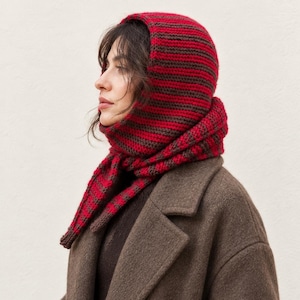 Könnte beinhalten: Eine gestrickte Kapuzen-Schal-Kombination mit horizontalen Streifen in abwechselndem Dunkelbraun und leuchtendem Rot. Das Accessoire bedeckt den Kopf und wird um den Hals gewickelt, wobei es ein durchgehendes, strukturiertes Rippenstrickmuster aufweist.