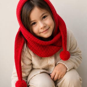May include: A bright red knitted hood with a long scarf-like extension on each side, featuring a round pom-pom attached to the end of each tail. The hood is constructed with a textured garter stitch pattern and provides full head coverage.