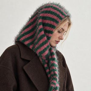 Puede incluir: Un pasamontañas de punto con textura difusa y rayas horizontales alternas en verde oscuro y rosa empolvado. Esta prenda para la cabeza cae por los lados y está confeccionada con un hilo suave y cepillado que crea un aspecto texturizado definido.
