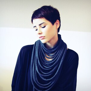 May include: A woman with short dark hair is wearing a dark blue infinity scarf. The scarf is made of a soft, stretchy fabric and is worn around the neck.